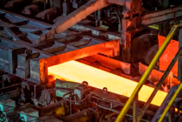 Processo de fabricação de aço com uma barra de metal incandescente saindo de um forno industrial, rodeada por complexas estruturas metálicas.