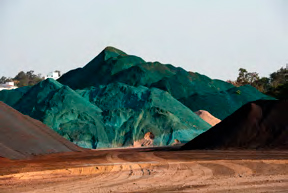 Montes de minério coloridos em tons vibrantes de azul e verde, localizados em um depósito ao ar livre.