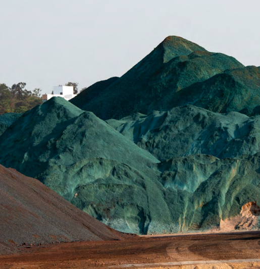 Montanhas de minério em tons vibrantes de verde-azulado sob um céu claro.